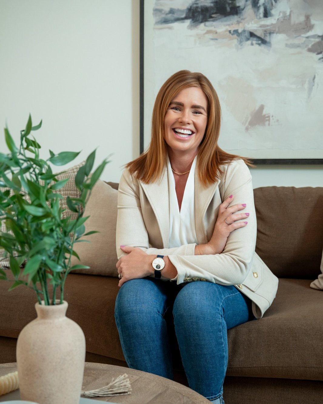 Lizzy, smiling, seated on a sofa with her arms crossed